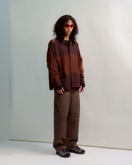 Person wearing a brown plaid shirt and pants standing against a plain background