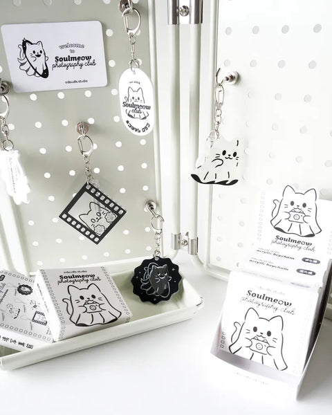 Collection of black and white cat-themed keychains and cards on a polka dot background.