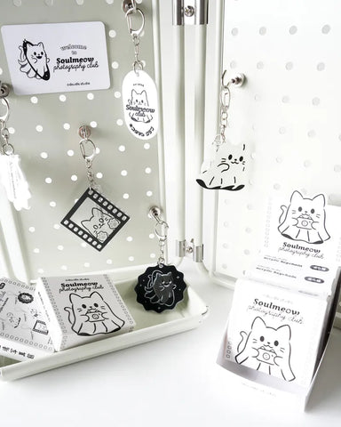 Collection of black and white cat-themed keychains and cards on a polka dot background.