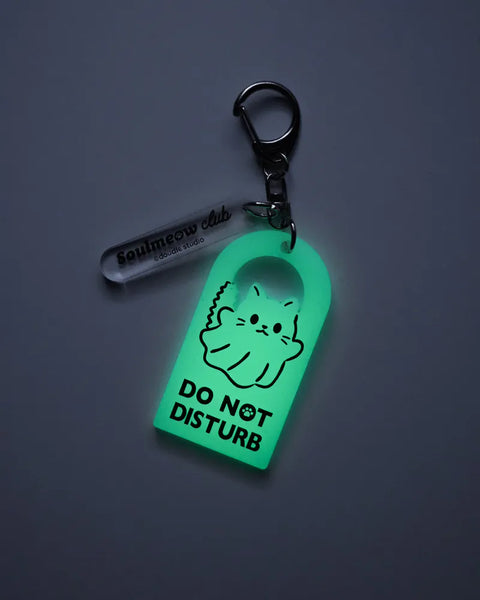 Glowing green keychain with 'Do Not Disturb' text and cartoon cat design on a dark background.