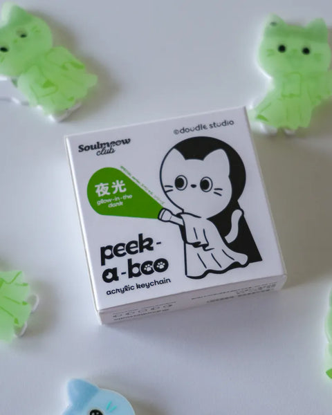 Box of 'peek-a-boo' acrylic keychain with cartoon cat design on a white background