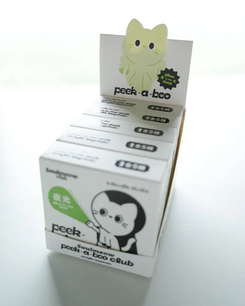 Display of Peek-a-Boo products with packaging and a small green toy on a white background