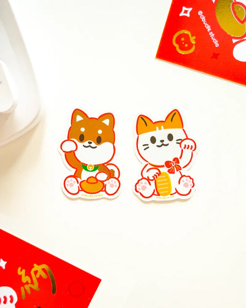 Two cartoon cat figurines with red envelopes on a white background
