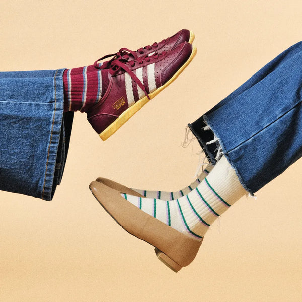 Two pairs of feet wearing different shoes and socks on a beige background