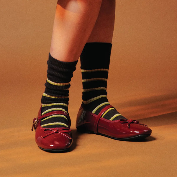 Person wearing black and yellow striped socks with red shoes on a brown background