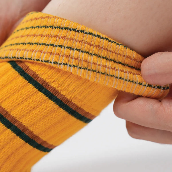 Close-up of a hand holding a yellow sock with green stripes.