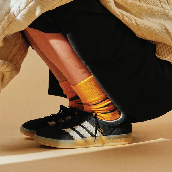 Person wearing black Adidas sneakers with yellow socks on a beige background