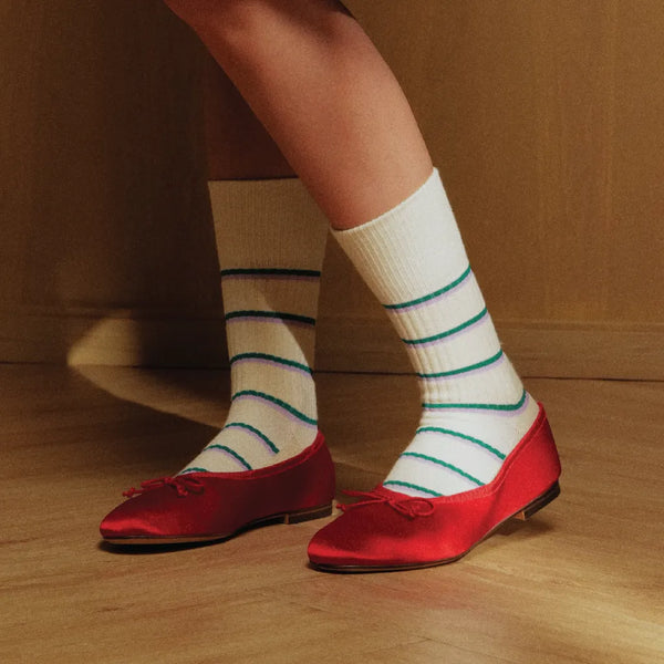 Red shoes with white socks featuring blue and green stripes on a wooden floor.
