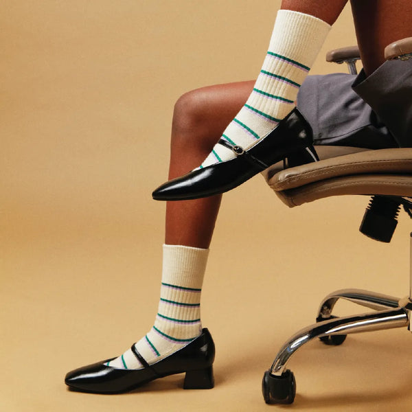 Person wearing white socks with blue stripes and black shoes sitting on a chair.