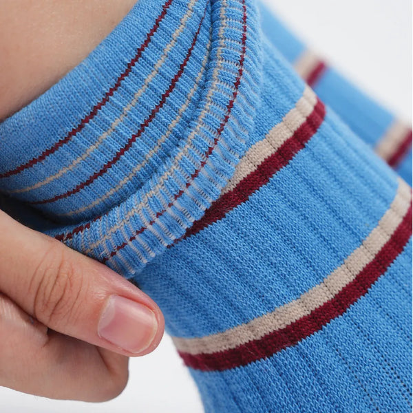 Close-up of a blue sock with red and beige stripes held by a hand.