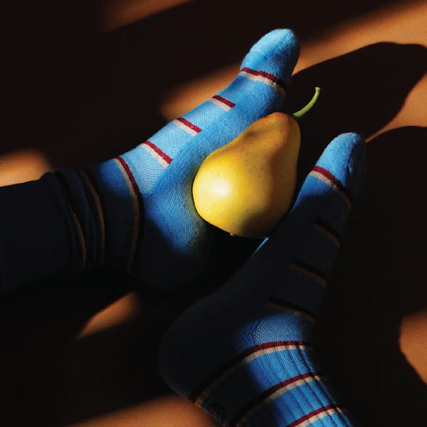 Person wearing blue socks with red stripes holding a pear.