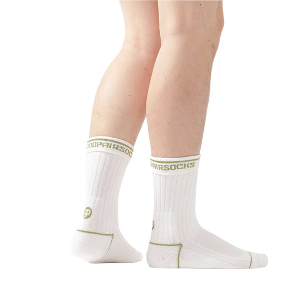 A pair of white GOODPAIR socks with green and black branding, worn on a person's legs, showcasing the ribbed texture and seamless toe closure.