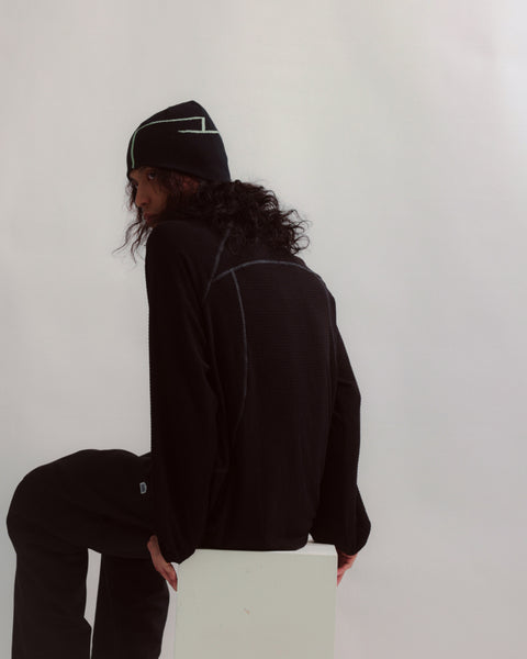 Person wearing a black outfit with a beanie against a white background