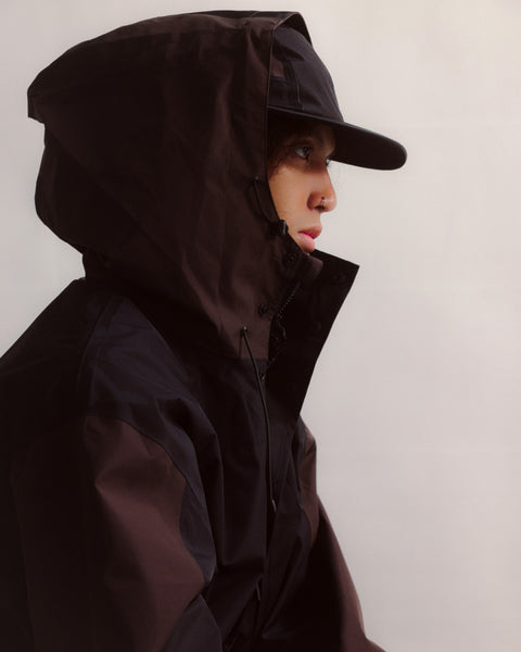 Person wearing a dark hooded jacket and cap against a plain background