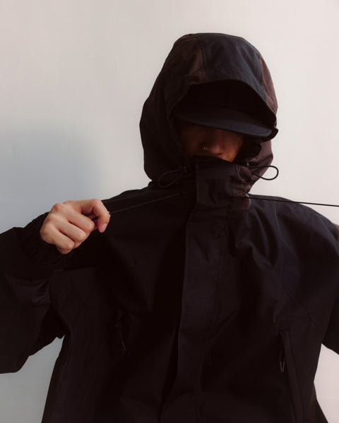 Person wearing a black hooded jacket against a plain background