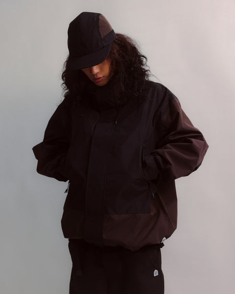 Person wearing a dark brown jacket and hat against a plain background