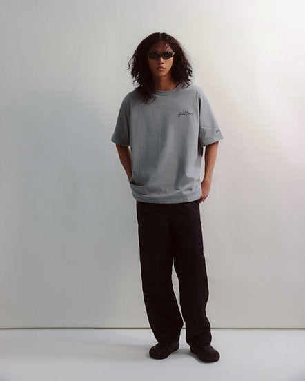 Person wearing a gray oversized t-shirt and black pants on a white background