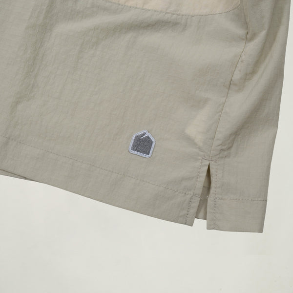 Close-up of beige shorts with a brand logo on a light background