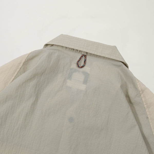 Close-up of a beige and green jacket with a brand logo on a light gray background