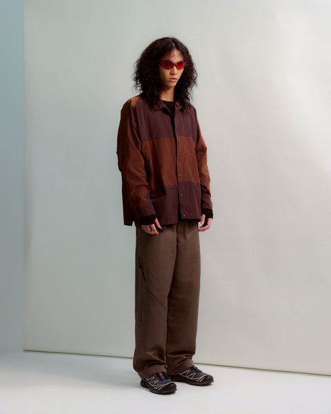 Person wearing a brown jacket and pants standing against a plain background