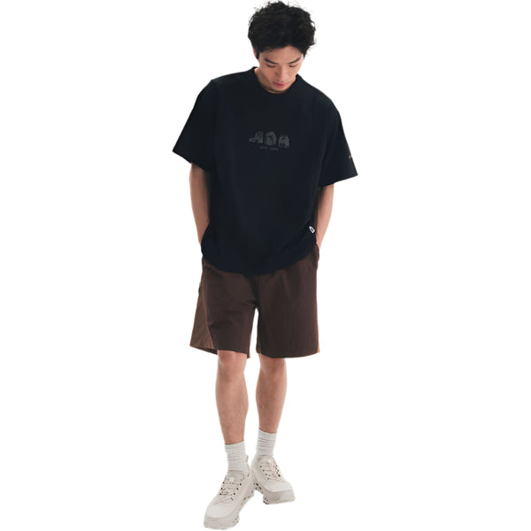 Person wearing a black t-shirt with a logo and brown shorts on a white background