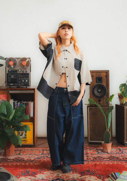 Person wearing a stylish outfit with a cap in a room with vintage speakers and decor.