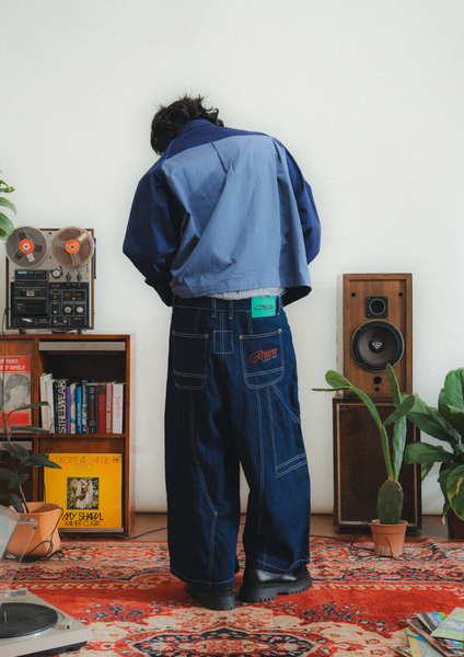 Person wearing a blue jacket and jeans standing in a room with vintage speakers and records.