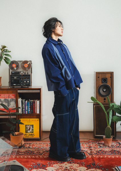 Person wearing a blue outfit standing in a room with vintage speakers and books.