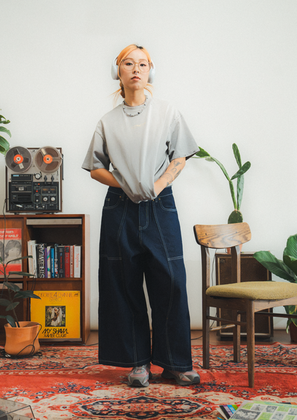 Person wearing a gray shirt and dark pants in a room with a vintage radio and books.
