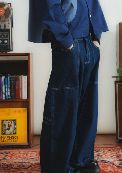 Person wearing blue denim overalls in a room with a bookshelf and records.