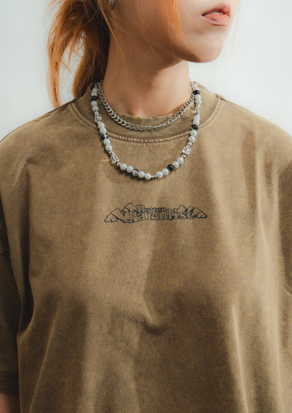 Person wearing a brown t-shirt with a logo and a beaded necklace.