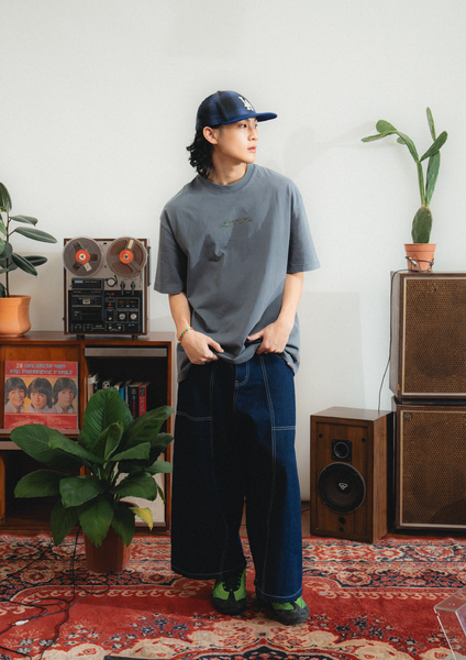 Person wearing a gray t-shirt and blue jeans standing in a room with vintage furniture and plants.