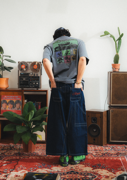 Person wearing a graphic t-shirt and dark jeans in a room with vintage equipment and plants.