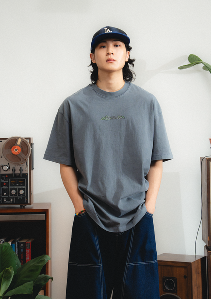 Person wearing a gray t-shirt and blue cap indoors with a white wall background