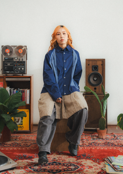 Person wearing a blue shirt and beige pants in a room with vintage speakers and plants.