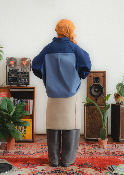 Person wearing a blue and gray jacket in a room with vintage speakers and decor