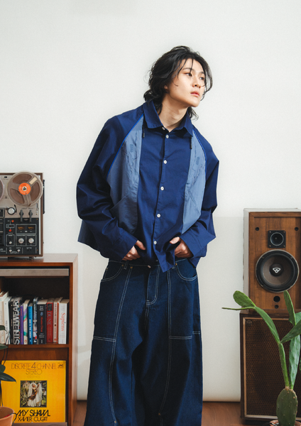 Person wearing a blue outfit standing in a room with vintage speakers and books.