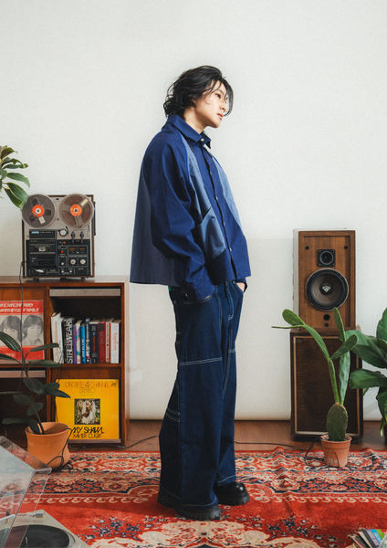 Person wearing a blue outfit standing in a room with vintage speakers and a reel-to-reel tape player.