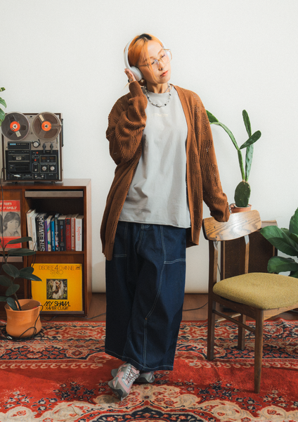 Person wearing headphones in a room with a vintage reel-to-reel tape recorder and books.