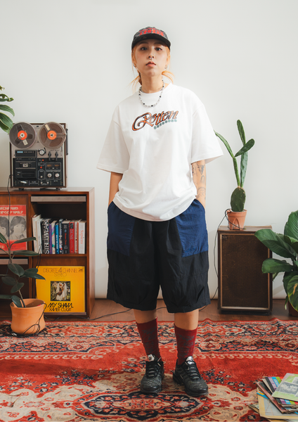 Person wearing a white t-shirt with colorful text and navy shorts in a room with plants and a vintage radio.