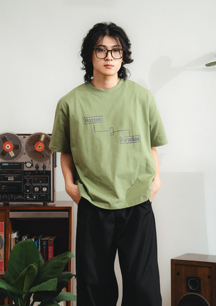 Person wearing a green t-shirt with text, standing in a room with a vintage reel-to-reel tape recorder and speakers.