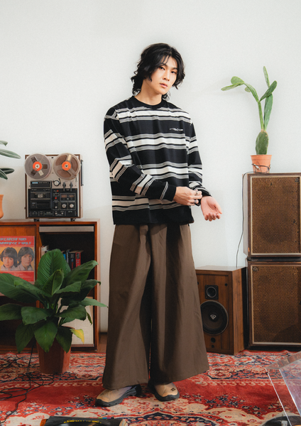 Person wearing a black and white striped sweater and brown pants in a room with vintage furniture and decor.