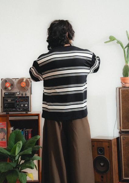Person wearing a black and white striped shirt in a room with vintage equipment and plants.