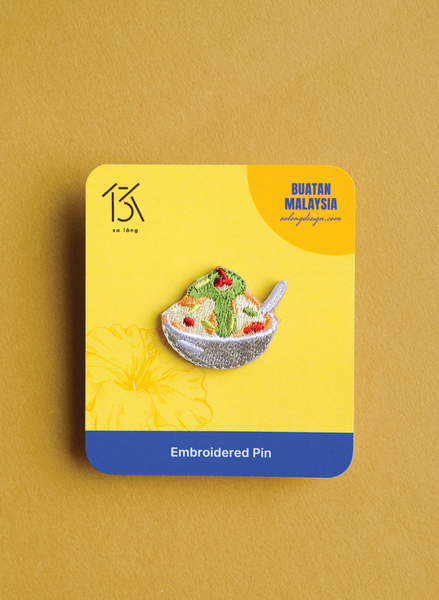 Embroidered pin on a yellow card with 'Buatan Malaysia' branding on a brown background