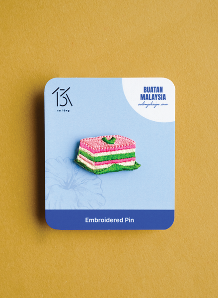Embroidered pin on a blue card with 'Buatan Malaysia' branding against a yellow background