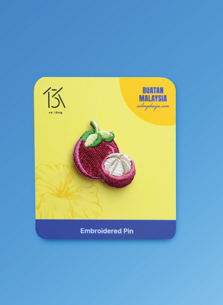 Embroidered pin of a passion fruit on a yellow card with 'Buatan Malaysia' branding against a blue background.