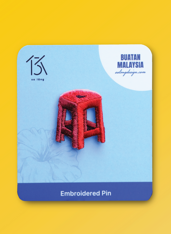 Embroidered pin of a red stool on a blue card with 'Buatan Malaysia' branding.