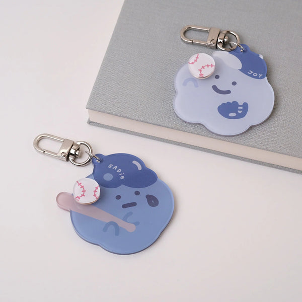 Two cartoon cloud keychains with facial expressions and baseballs on a light gray background.
