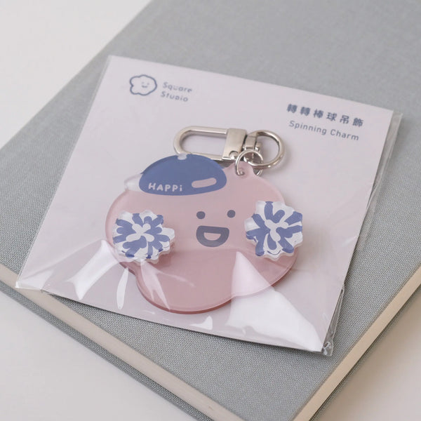Pink character keychain with blue accents on a white card, placed on a gray textured surface.