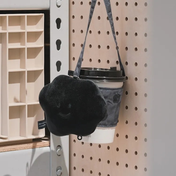 Black furry bag with a smiley face design hanging on a pegboard.